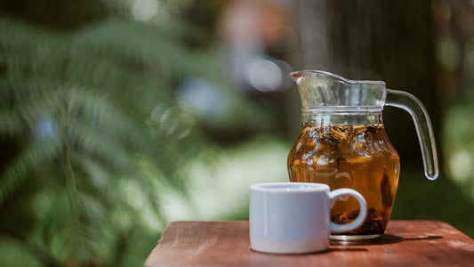 Glass pitcher of tea and a white cup on a wooden table